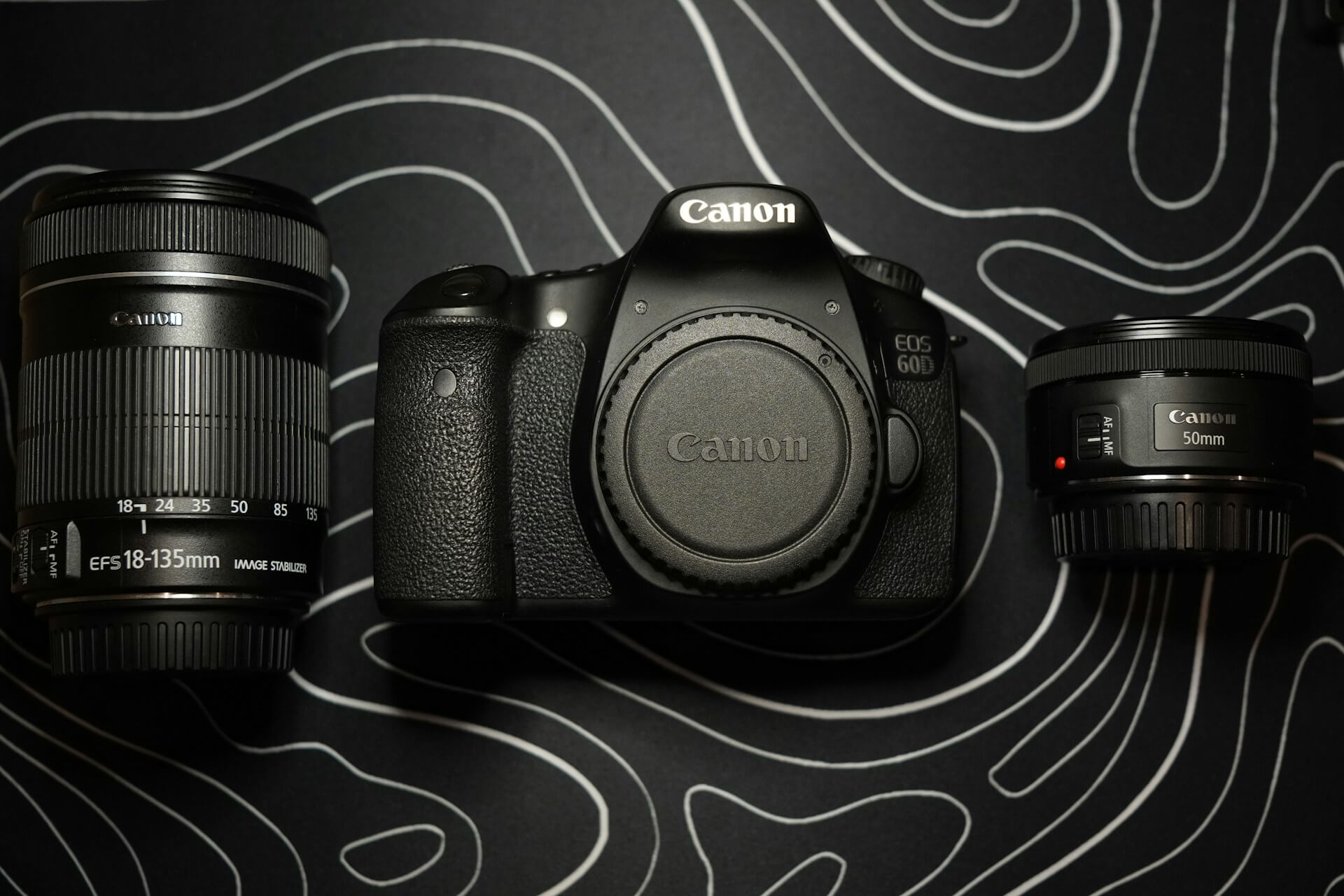 Canon EOS 60D váz 18-135mm és 50mm objektívekkel. Canon EOS 60D DSLR fényképezőgépváz felülnézetben egy Canon EF-S 18-135mm zoom- és egy EF 50mm f/1.8 prím objektív között.