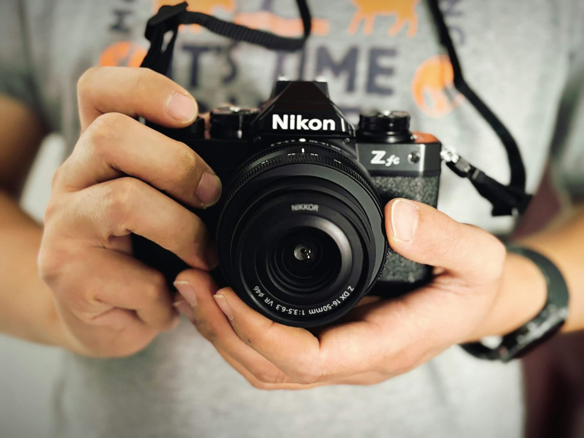 Nikon Z fc retro stílusú fényképezőgép kézben tartva. Szemből készült fotó egy kézben tartott, fekete vázas Nikon Z fc tükör nélküli fényképezőgépről, Nikkor Z DX 16-50mm VR objektívvel.