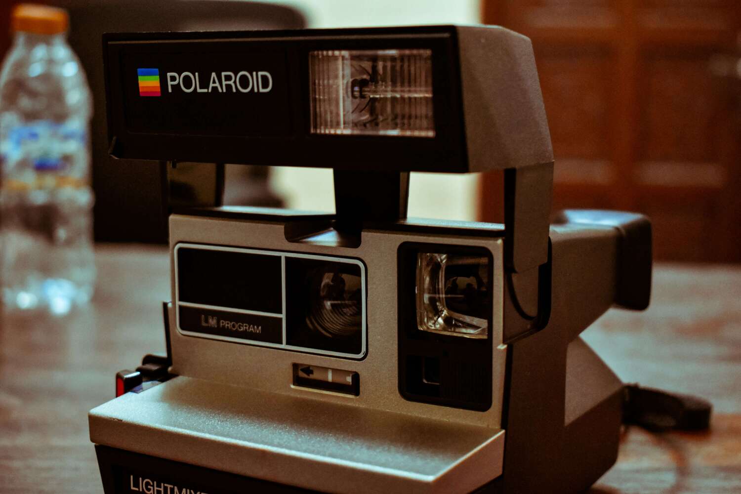 Klasszikus Polaroid 600 instant fényképezőgép beépített vakuval. Közelkép egy szürke és fekete színű, felnyitott vakus Polaroid 600-as sorozatú instant fényképezőgépről egy faasztalon.