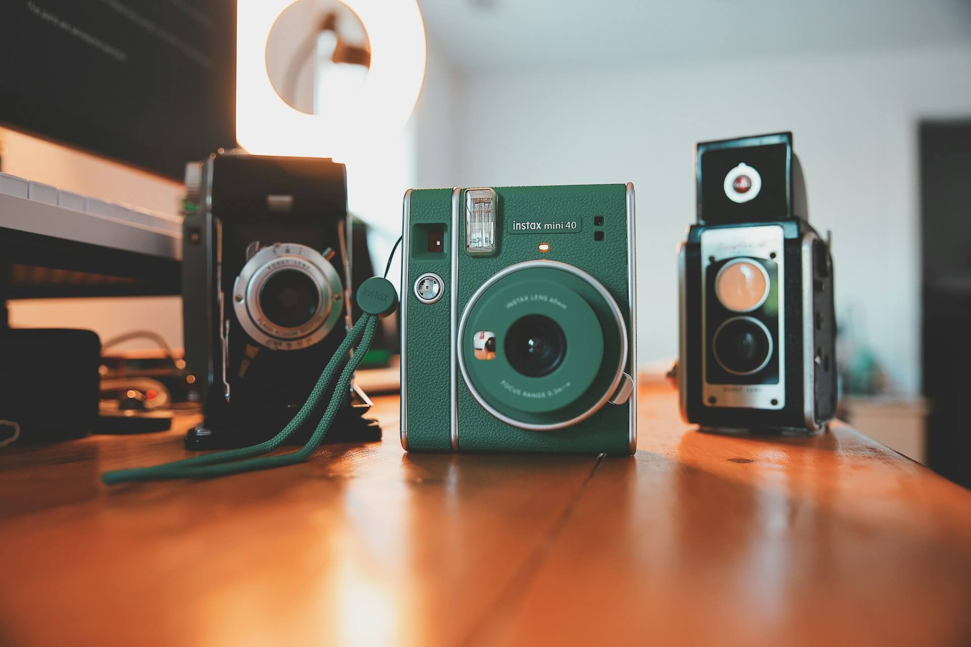 Zöld színű Fujifilm Instax Mini 40 instant fényképezőgép egy faasztalon, vintage analóg kamerákkal a háttérben.