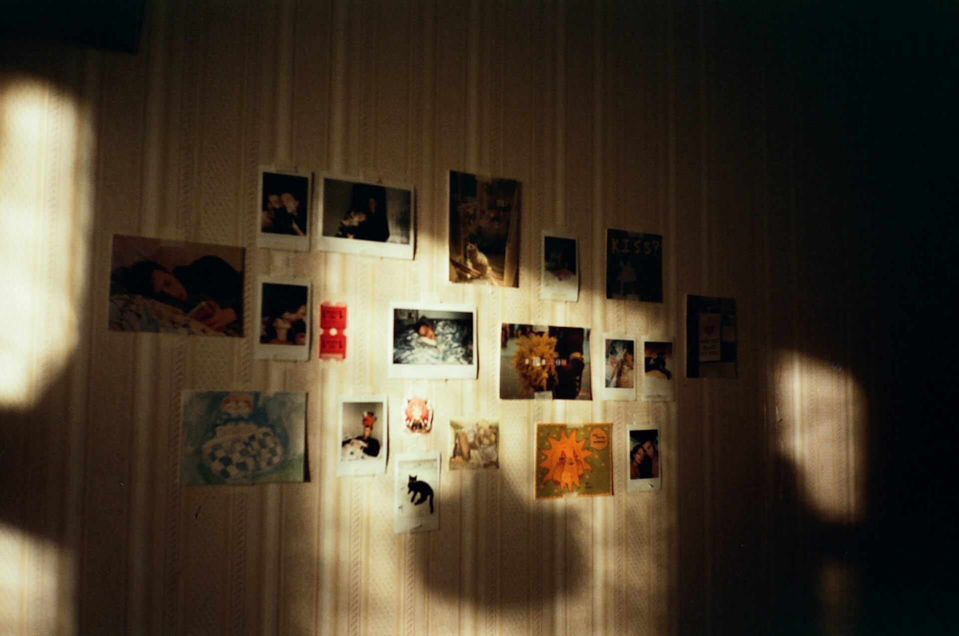 Napfényes szobafal személyes fotókkal, Instax képekkel és emlékekkel. Tapétázott szobafal vintage képekkel, Instax fotókkal és kis rajzokkal díszítve, amire meleg napfény vetül.