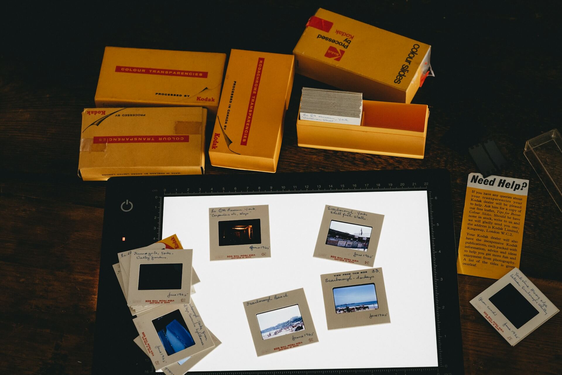 Analog diafilmek válogatása és archiválása átvilágító asztalon Kodak dobozokkal. Megvilágított LED átvilágító lapon elrendezett 35 mm-es keretezett diafilmek, mellette sárga Kodak diatároló dobozokkal.