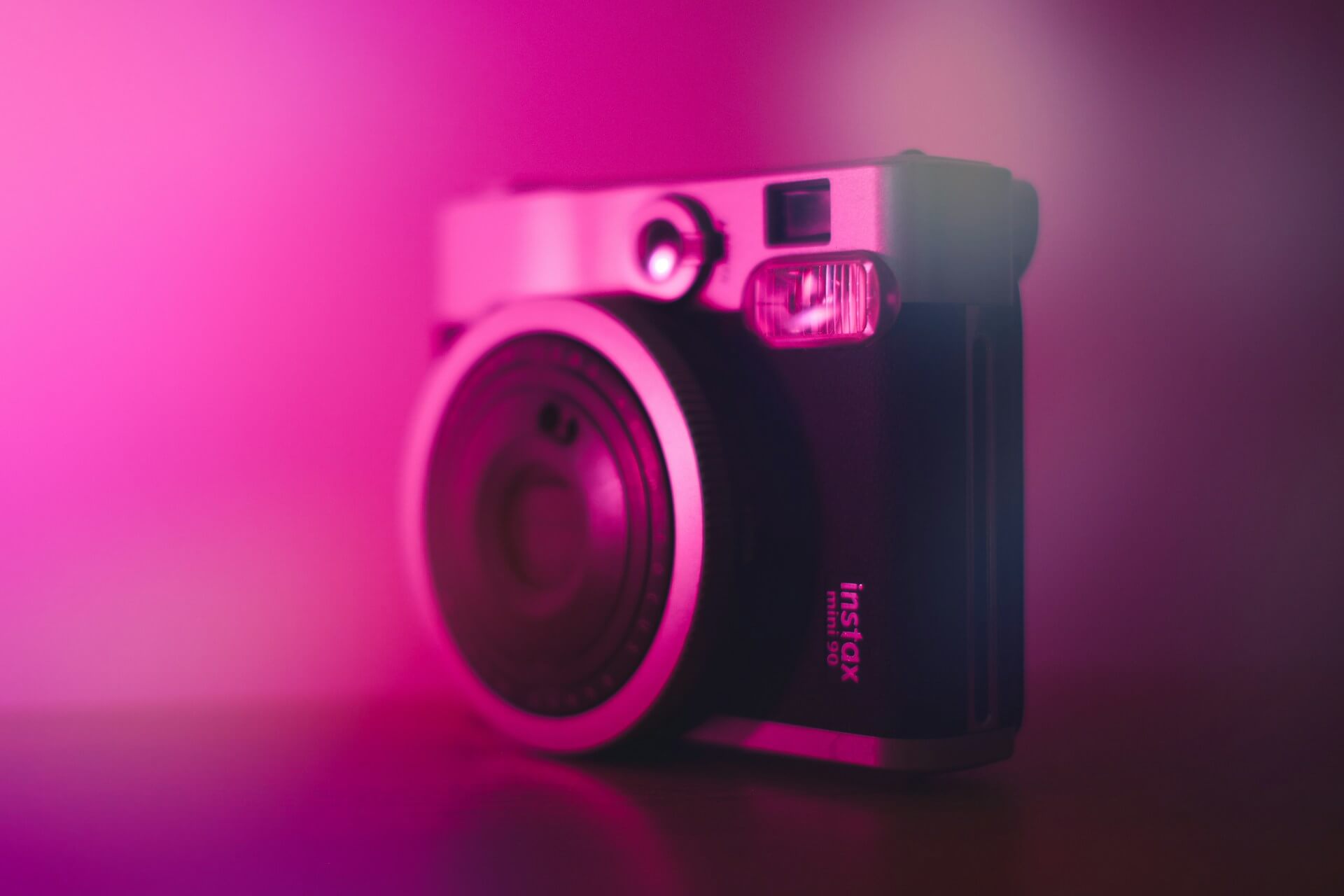 Fujifilm Instax Mini 90 fényképezőgép lila neoni fényben. Egy fekete-ezüst Fujifilm Instax Mini 90 Neo Classic instant fényképezőgép élénk rózsaszín és lila fényben megvilágítva.