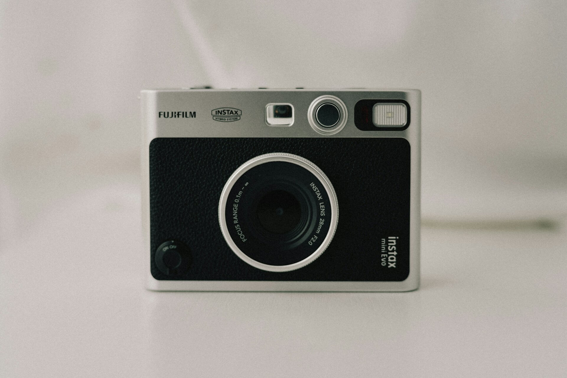 Fujifilm Instax Mini Evo hibrid instant fényképezőgép. Retro stílusú, ezüst és fekete Fujifilm Instax Mini Evo hibrid instant fényképezőgép szemből, világos háttér előtt.