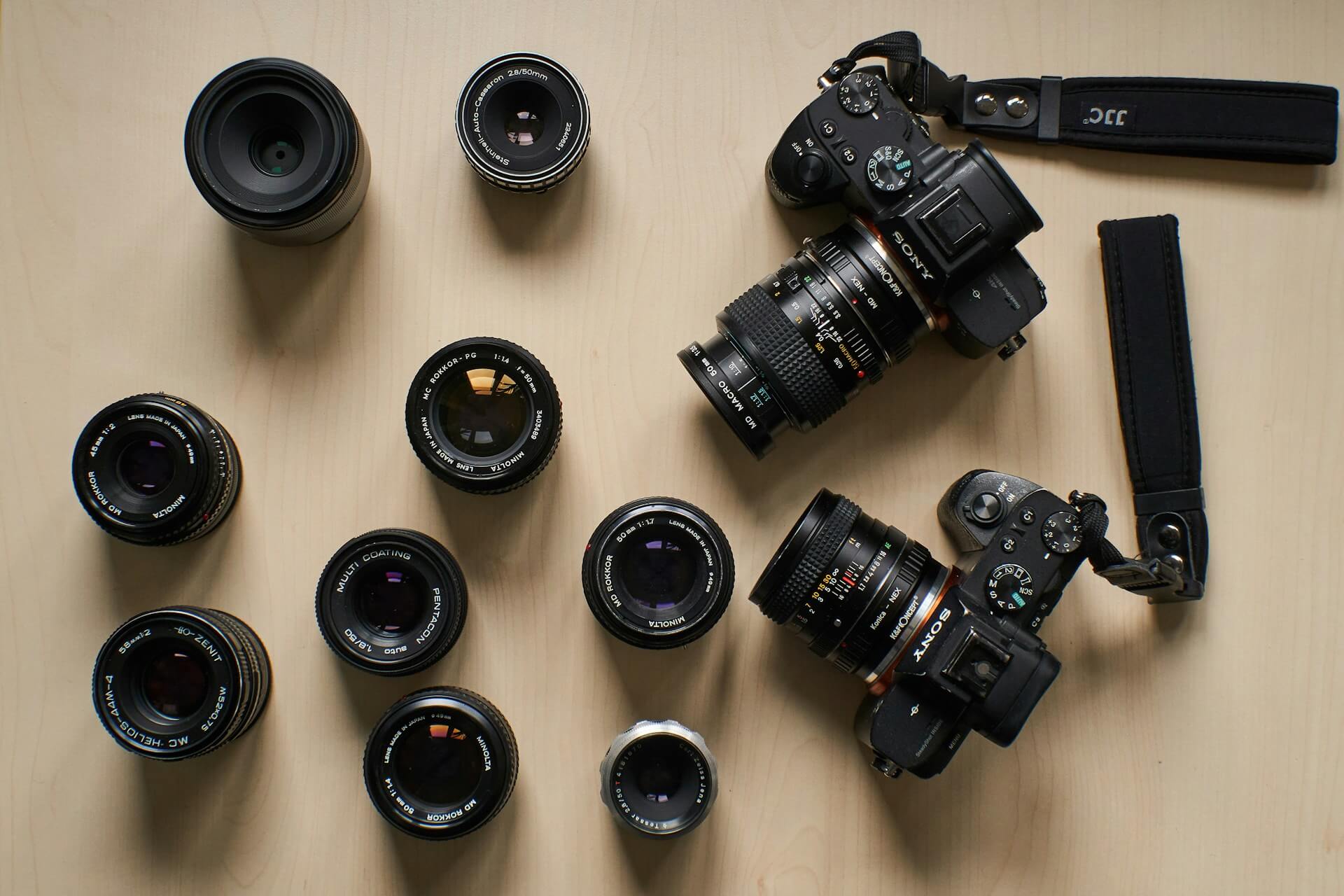 Sony vázak és manuális vintage objektívek gyűjteménye faasztalon. Felülnézeti fotó világos faasztalra elrendezett Sony tükör nélküli vázakról és különféle klasszikus kézi élességállítású (Helios, Minolta, Pentacon) objektívekről.