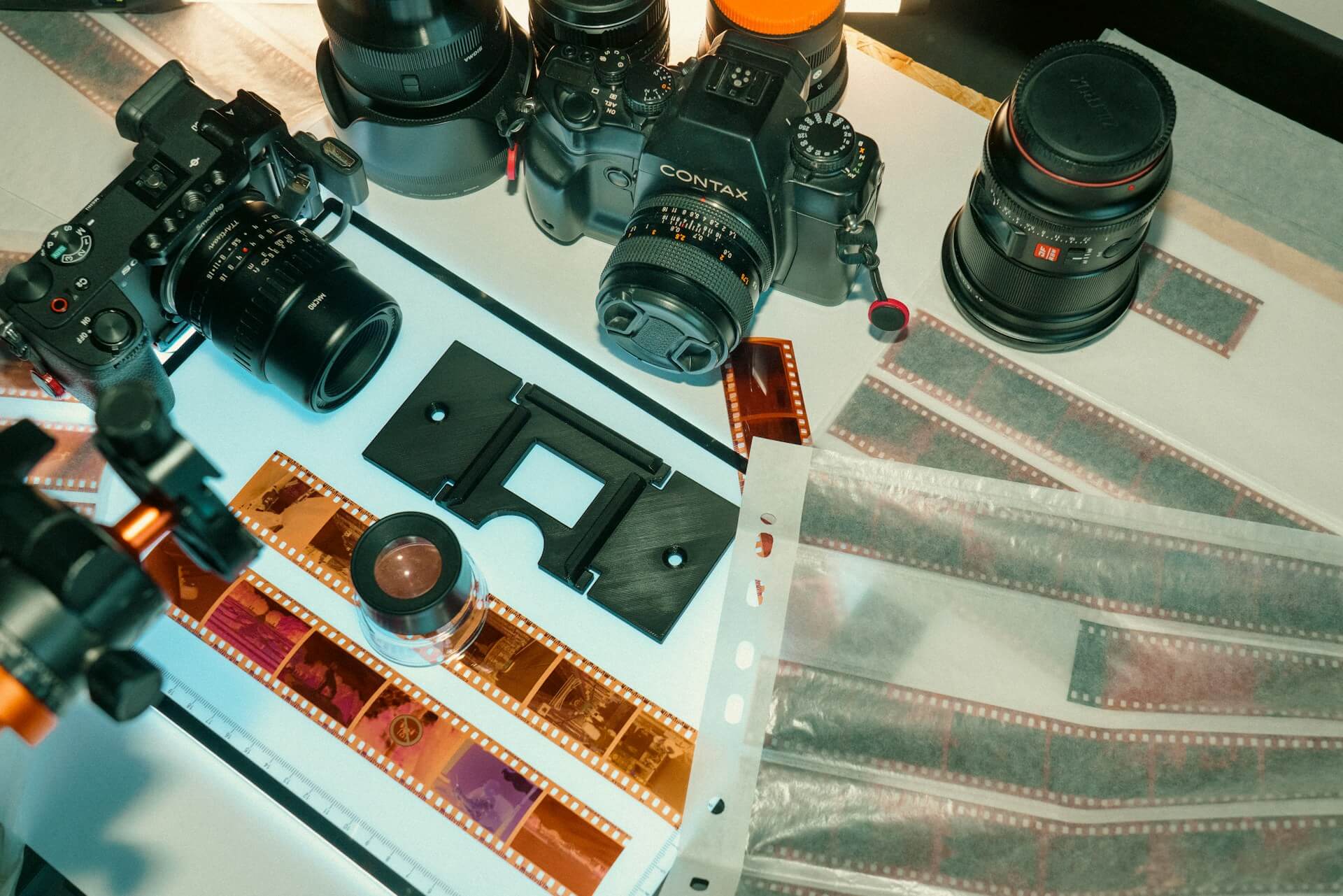 Felülnézeti kép átvilágító lapon lévő filmnegatívokról, Contax és Sony fényképezőgépekről, objektívekről és archiváló tasakokról.