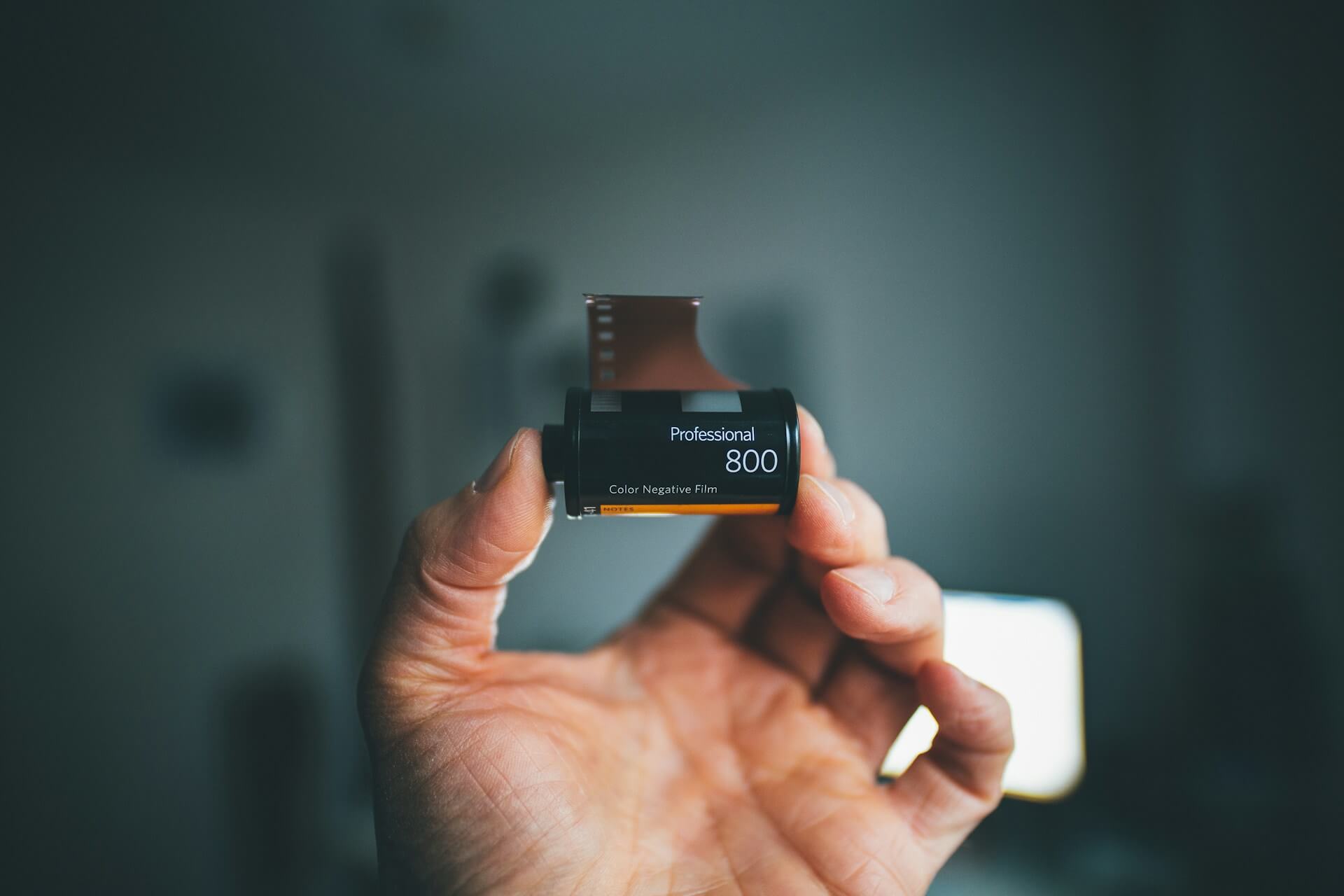 Egy férfi kézben tartott Professional 800-as típusú, 35 mm-es színes negatív filmtekercs félig kilógó filmcsíkkal.