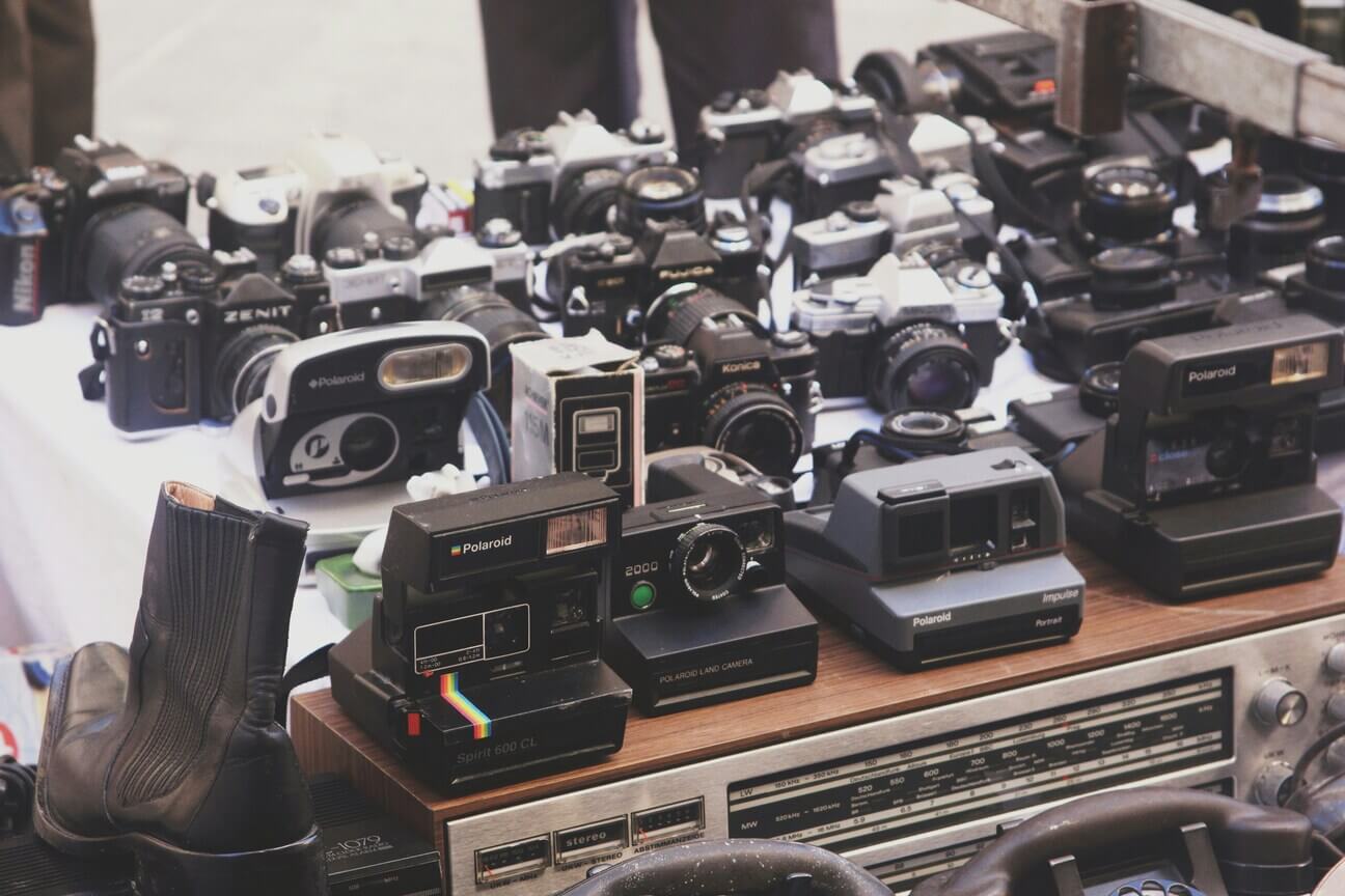Polaroidok és analóg gépek a vásárban Több Polaroid és analóg fényképezőgép egy bolhapiaci asztalon, régi rádió és egyéb tárgyak között
